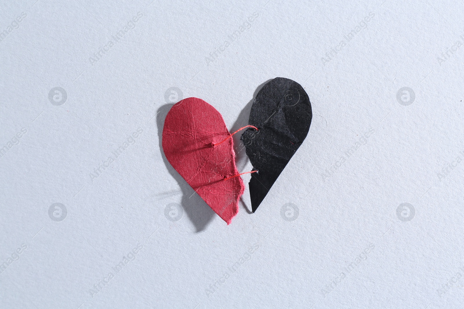 Photo of Halves of torn paper heart connected by thread on gray background, top view. Relationship problem concept