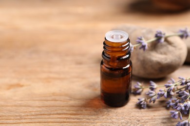 Bottle of essential oil and lavender flowers on wooden table, closeup. Space for text