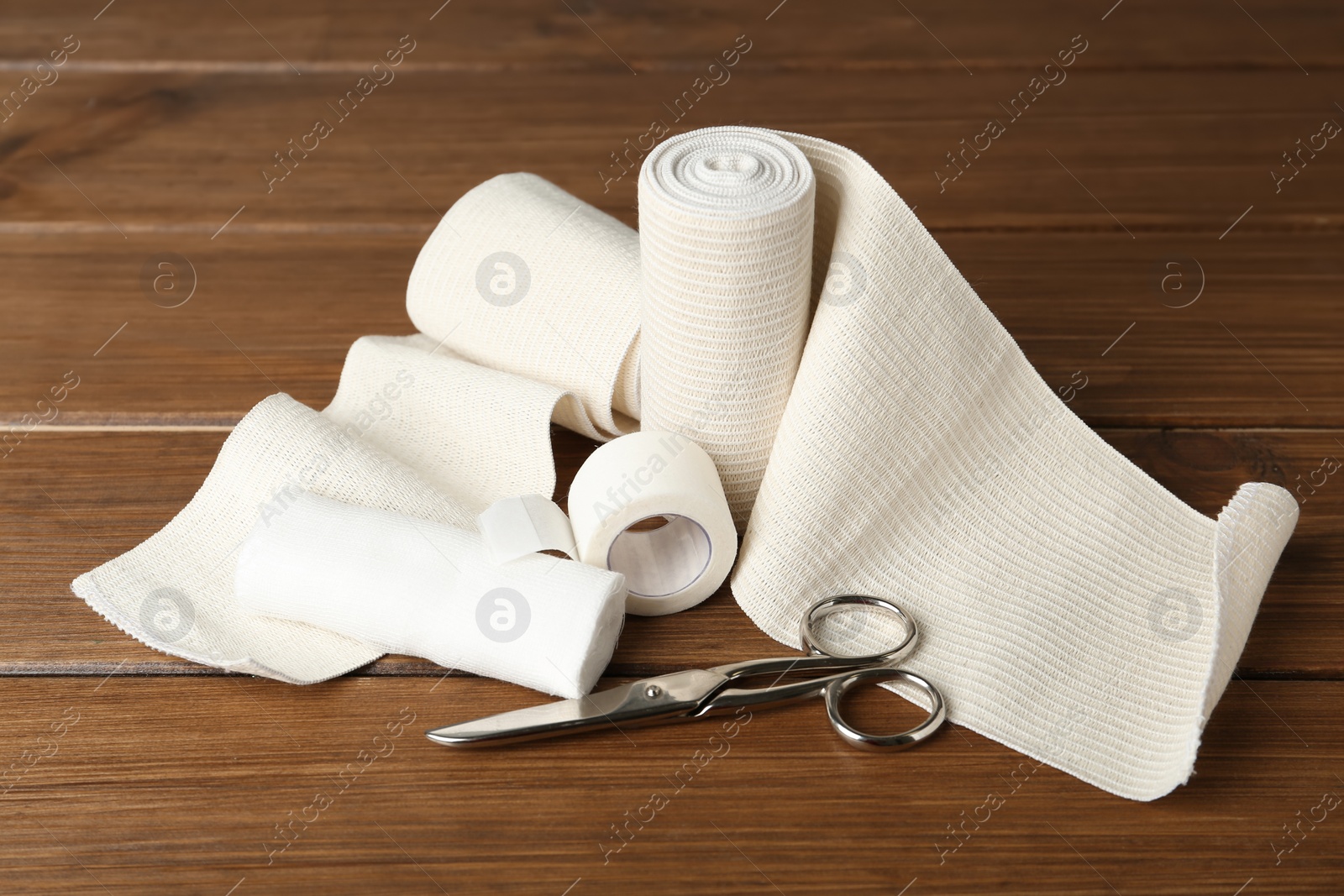 Photo of Medical bandage rolls, sticking plaster and scissors on wooden table