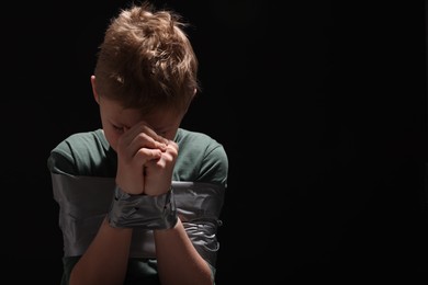 Photo of Little boy tied up and taken hostage on dark background. Space for text