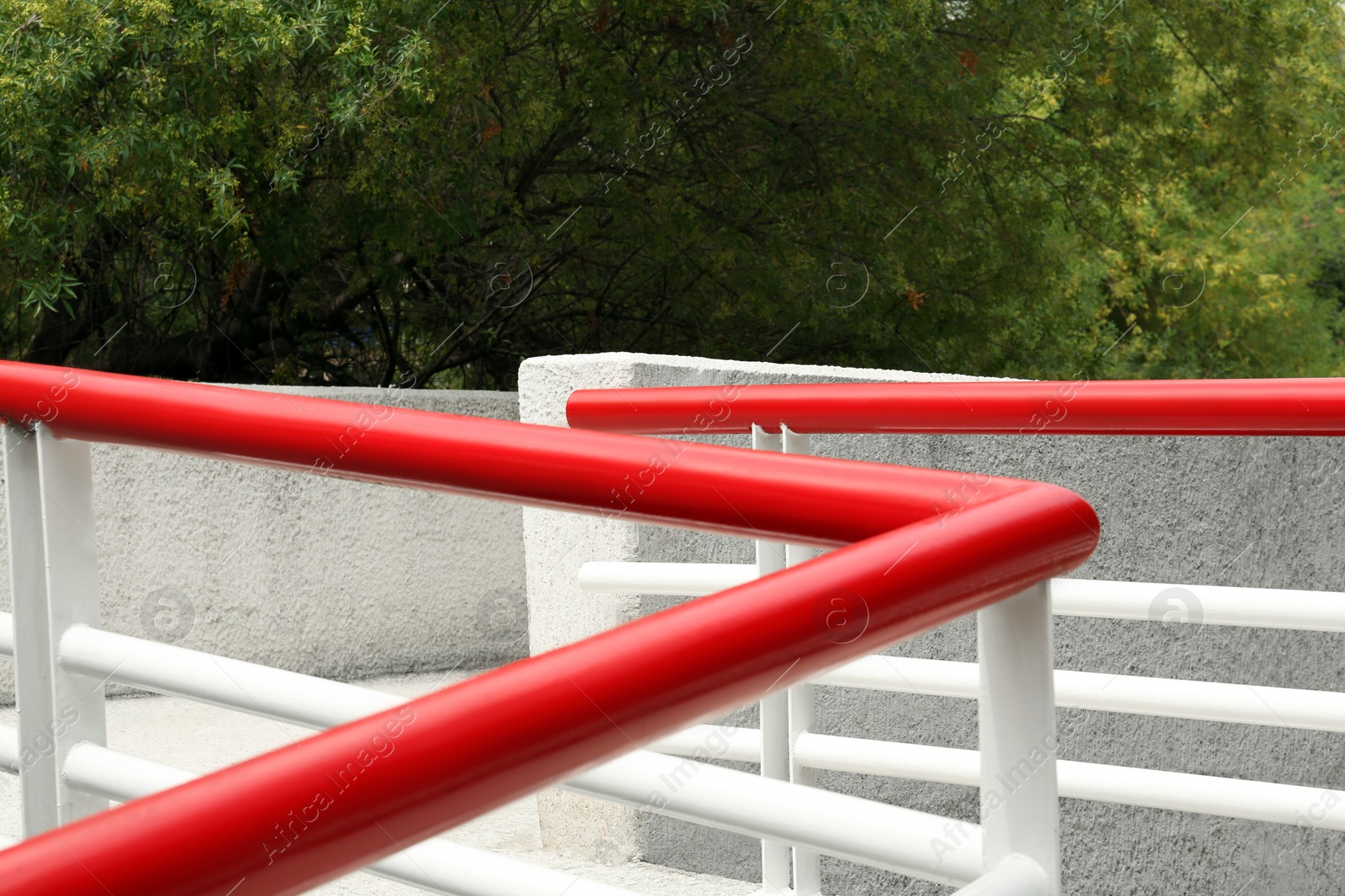 Photo of Ramp with red metal handrailings near trees outdoors