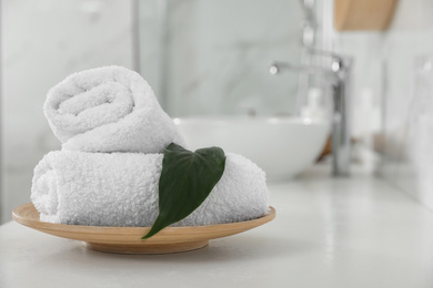 Photo of Rolled fresh towels and green leaf on white table in bathroom