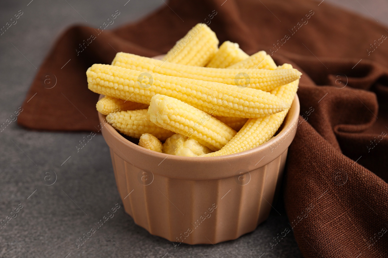 Photo of Tasty fresh yellow baby corns in bowl on brown table, closeup