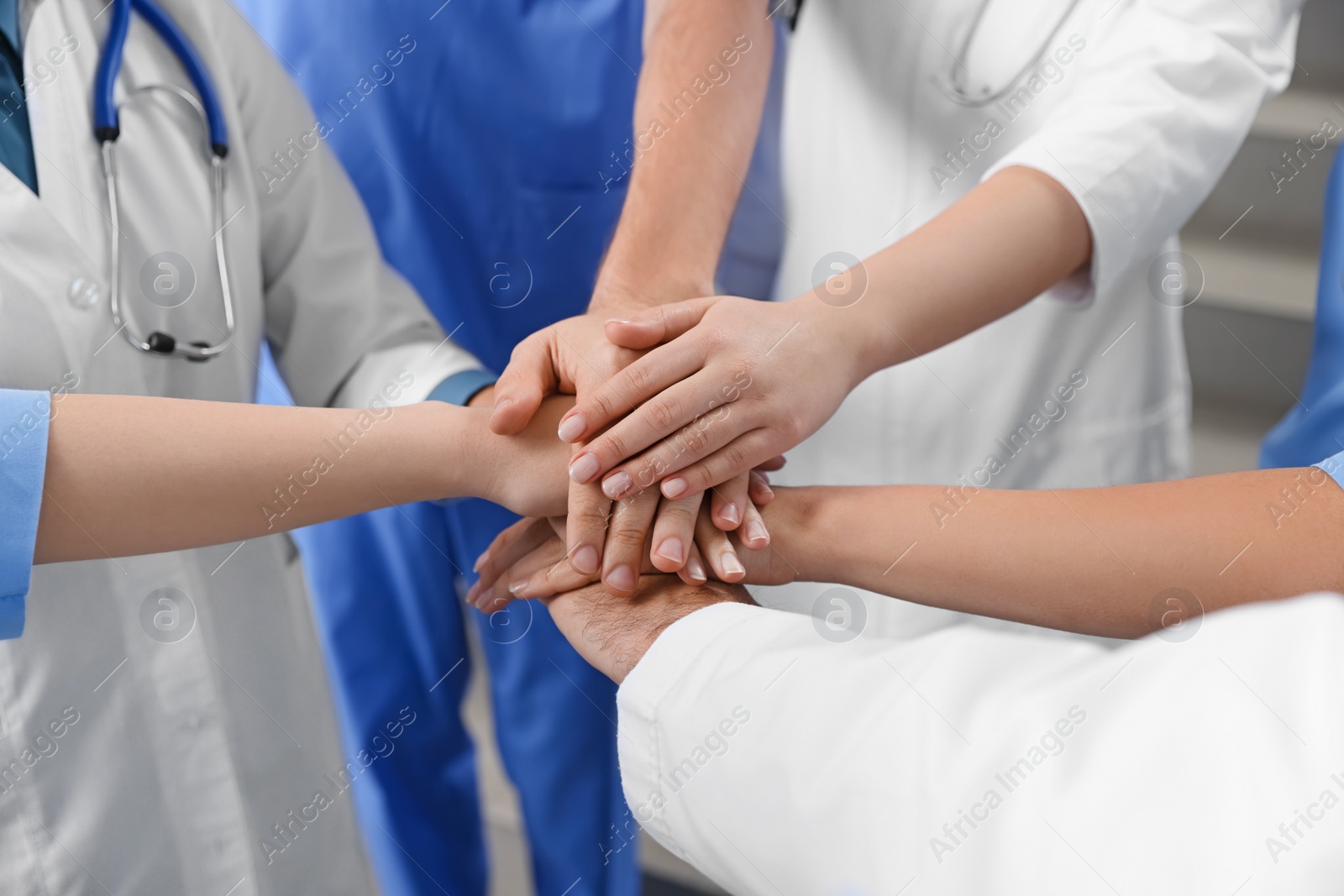 Photo of Team of medical doctors putting hands together indoors, closeup