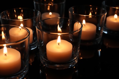 Photo of Wax candles burning on table in darkness, closeup