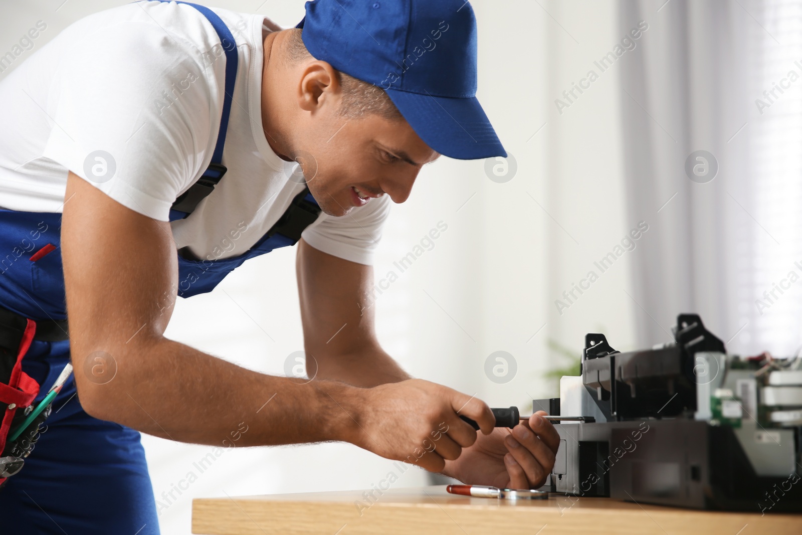 Photo of Repairman with screwdriver fixing modern printer in office