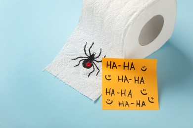 Photo of Toilet paper roll with drawn spider and words Ha-Ha  on light blue background. Celebrating April Fool's Day