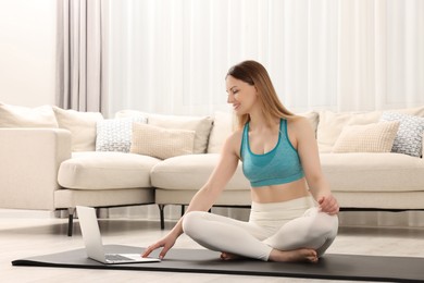 Photo of Woman in sportswear meditating near laptop at home