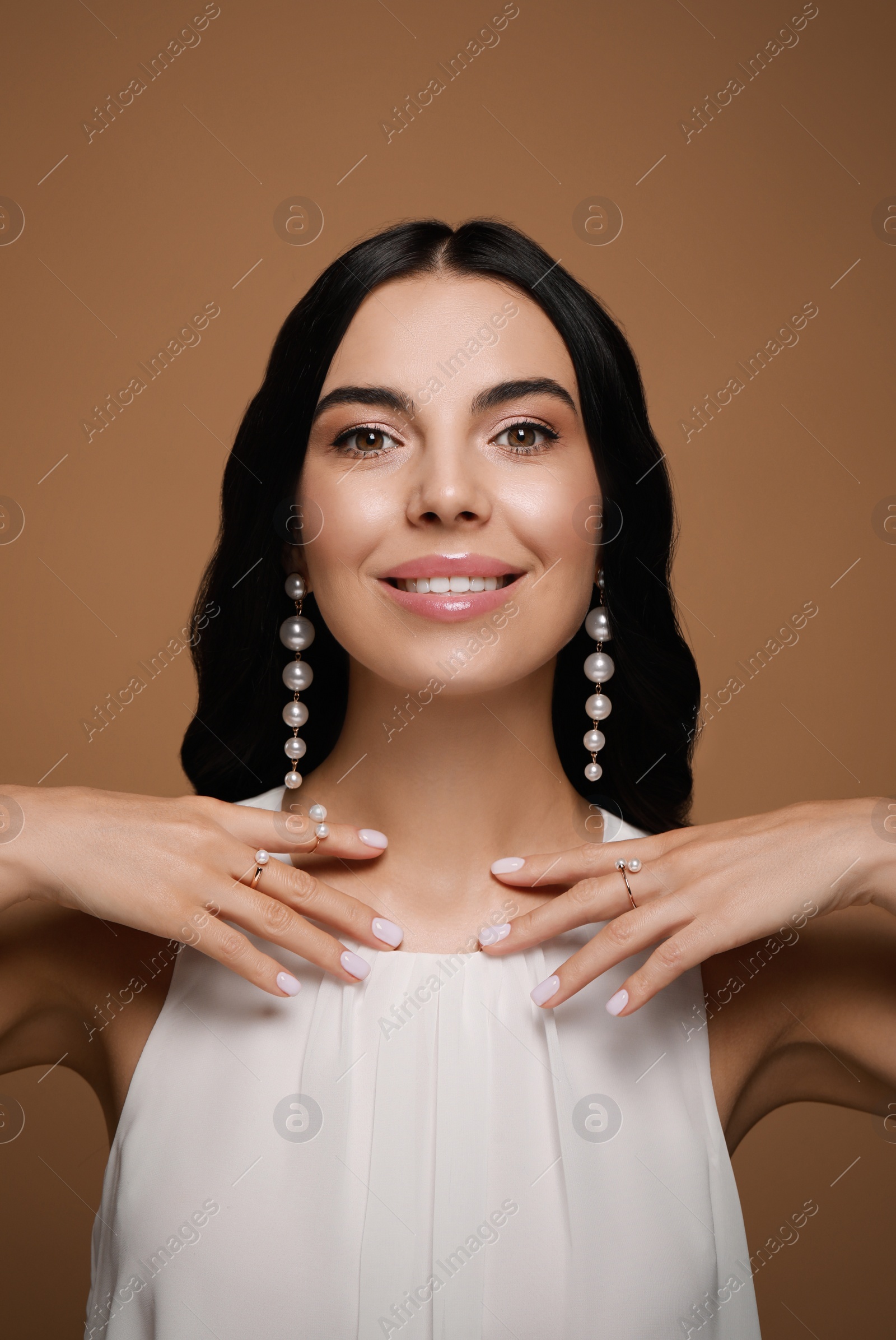 Photo of Young woman wearing elegant pearl jewelry on brown background