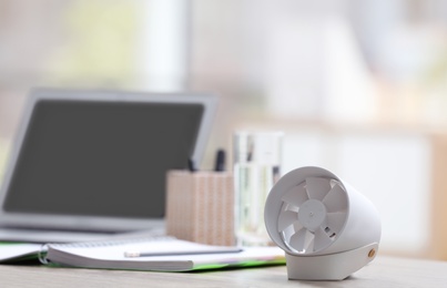 Modern portable fan on wooden table in office, space for text. Summer heat