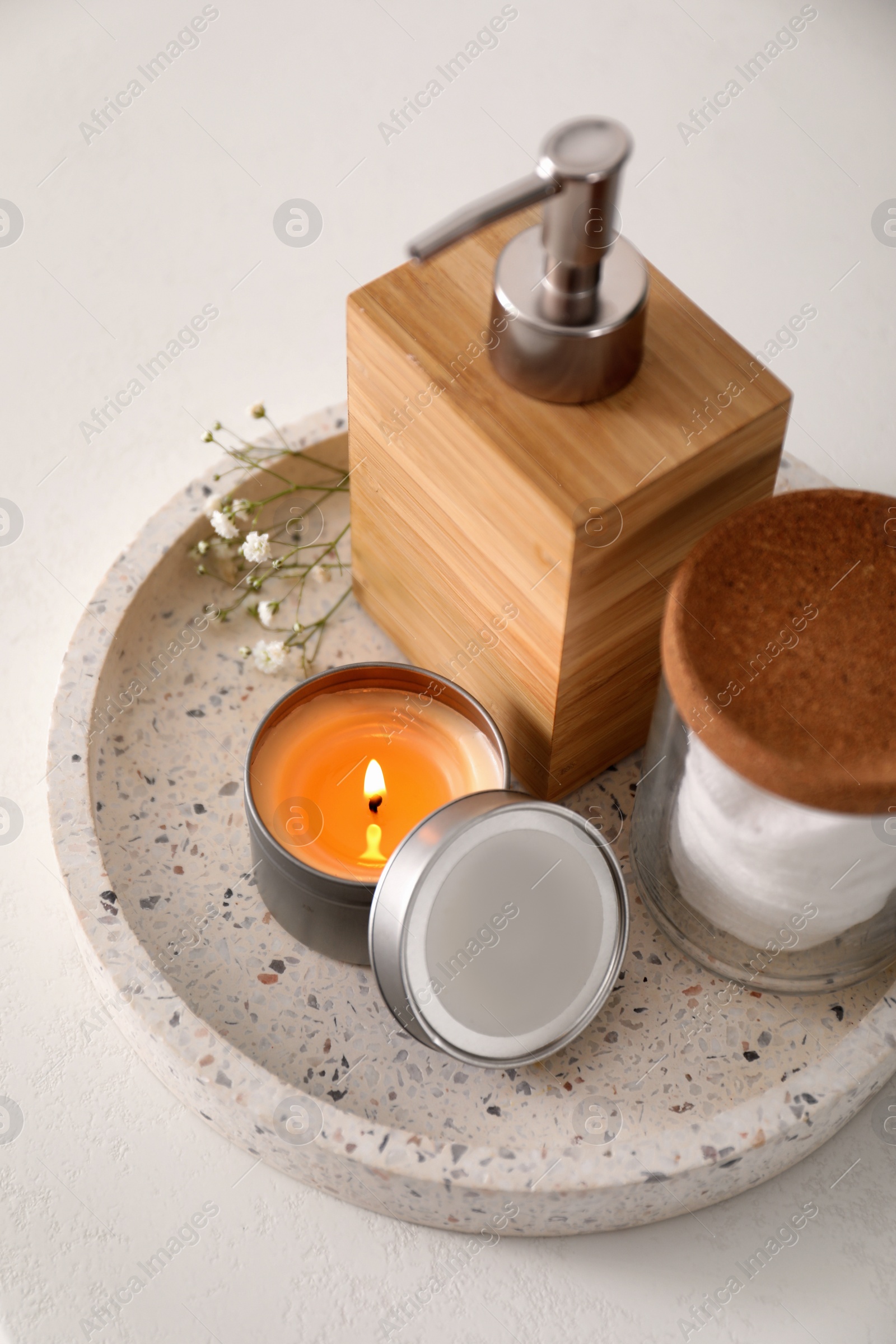 Photo of Tray with soap dispenser, cotton pads and burning candle on countertop in bathroom