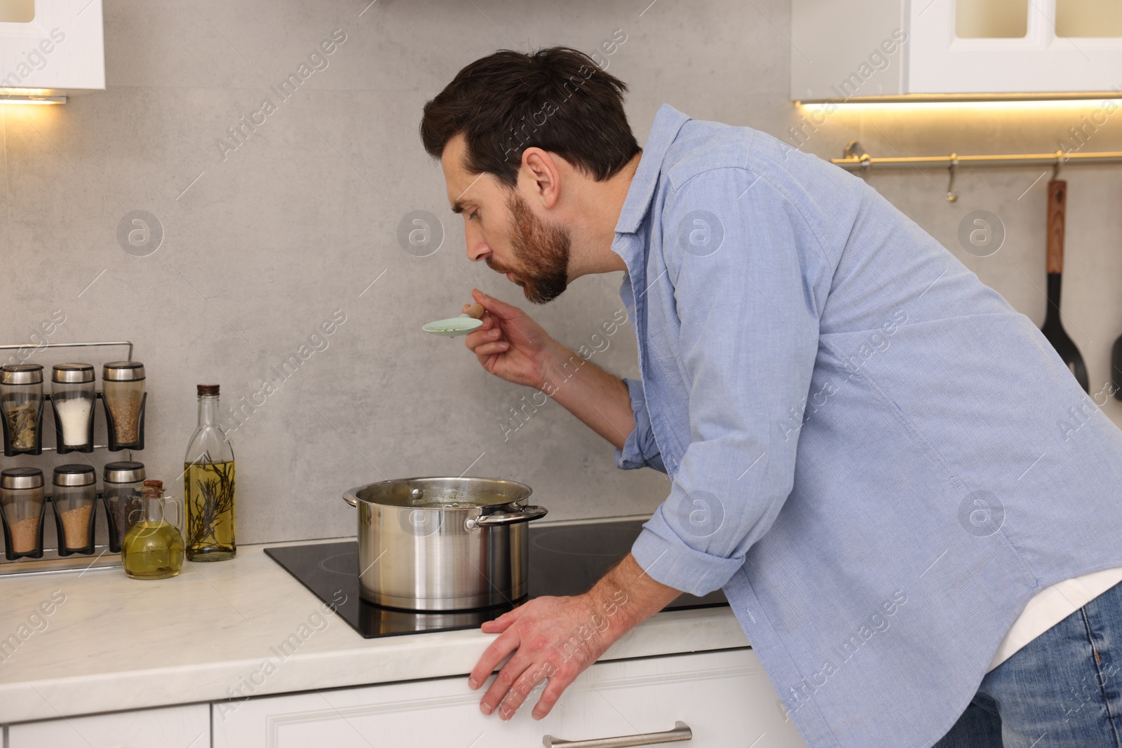 Photo of Man tasting delicious soup with spoon in kitchen