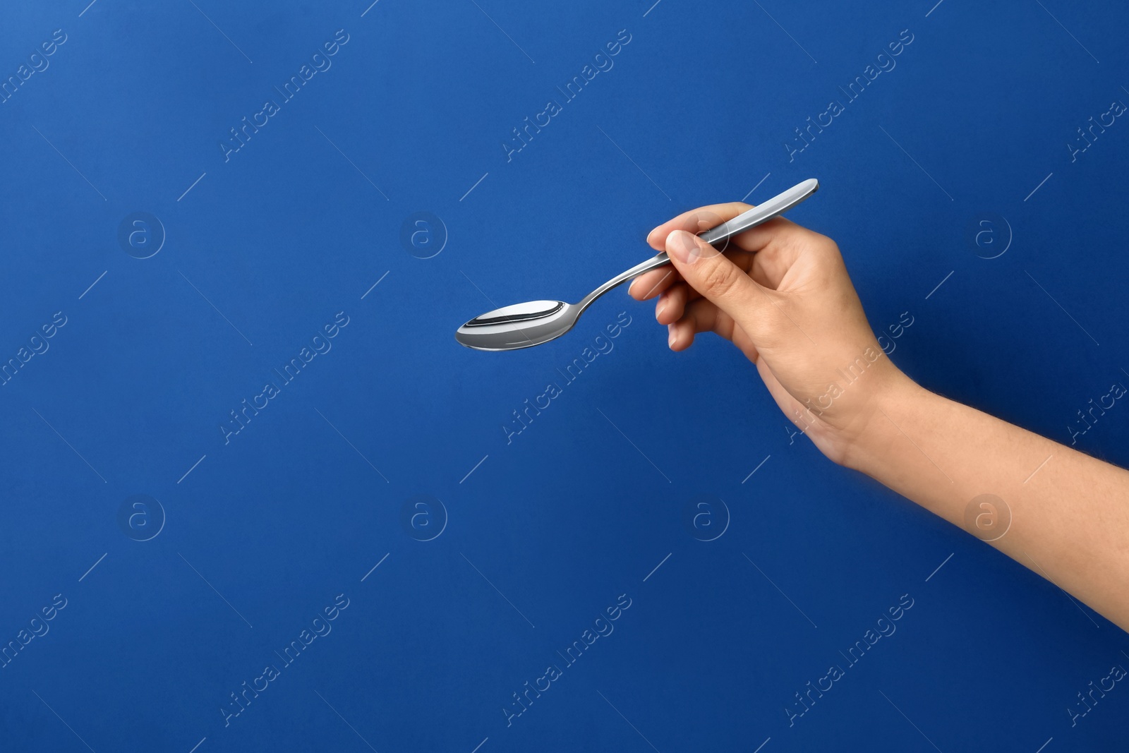 Photo of Woman holding empty table spoon on color background, closeup. Space for text