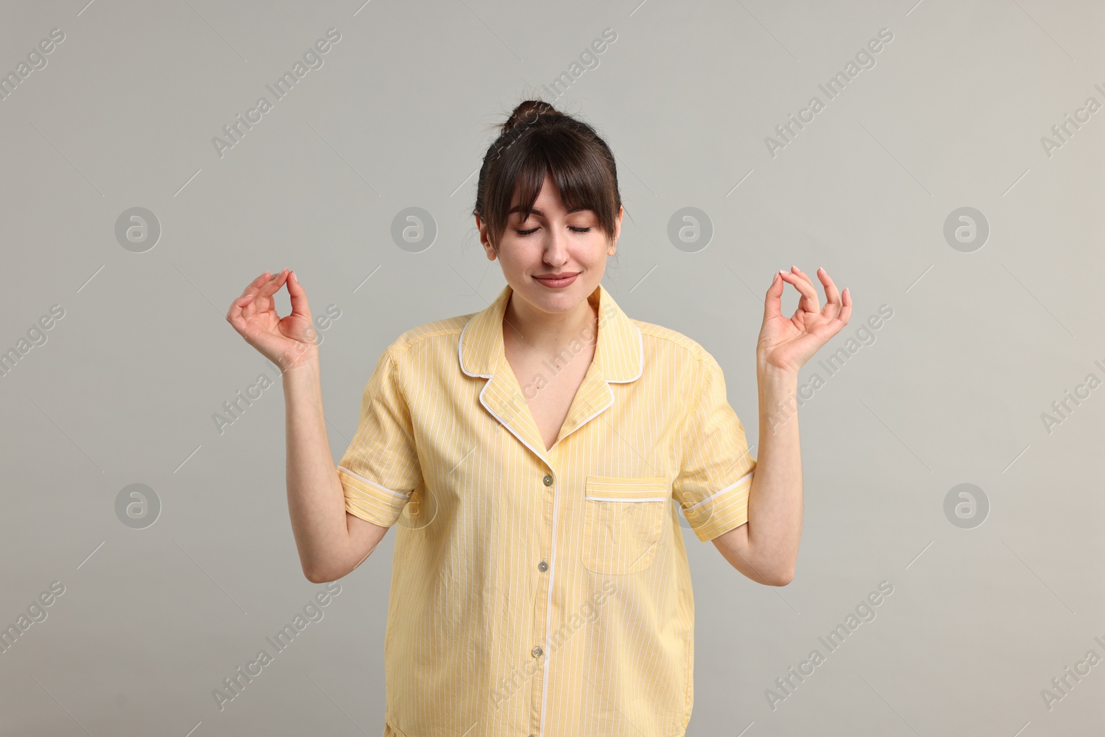 Photo of Woman in pyjama meditating on grey background