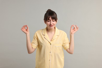 Woman in pyjama meditating on grey background