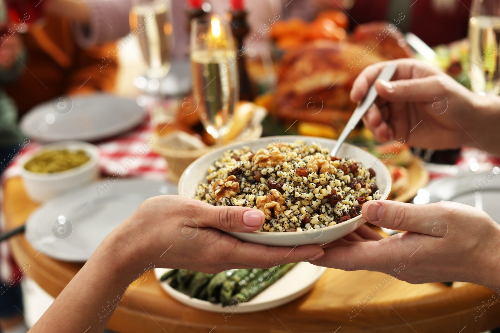 Photo of Woman giving bowl of traditional Christmas Slavic dish kutia to man at festive dinner, closeup