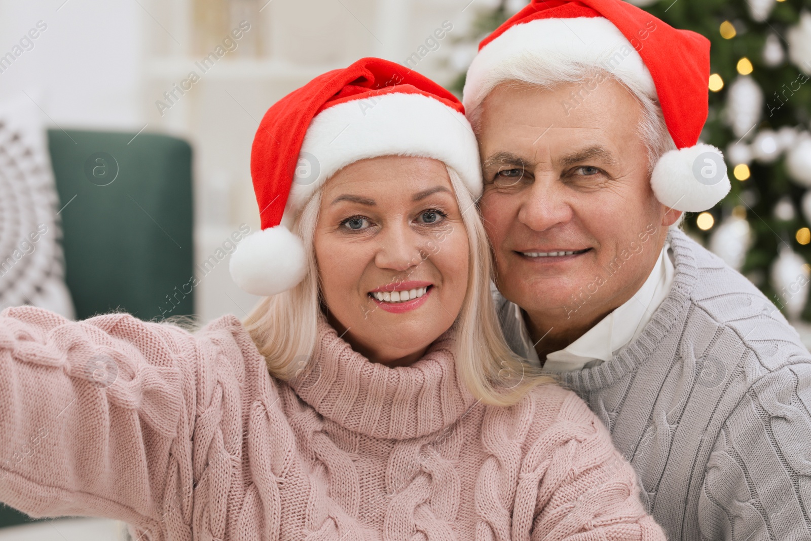 Photo of Happy mature couple in Santa hats taking selfie at home. Christmas celebration