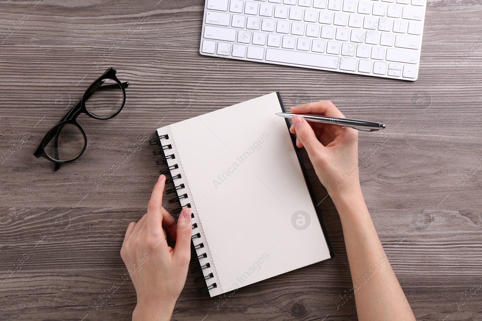 Photo of Woman writing in notebook at wooden table, top view