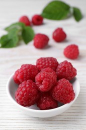 Photo of Tasty ripe raspberries in bowl on white wooden table. Space for text