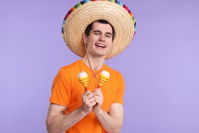 Photo of Young man in Mexican sombrero hat with maracas on violet background