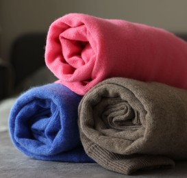 Photo of Rolled color sweaters on gray table, closeup