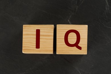 Photo of Wooden cubes with abbreviation IQ on black slate background, flat lay
