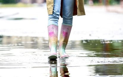 Woman with rubber boots in puddle, closeup. Rainy weather