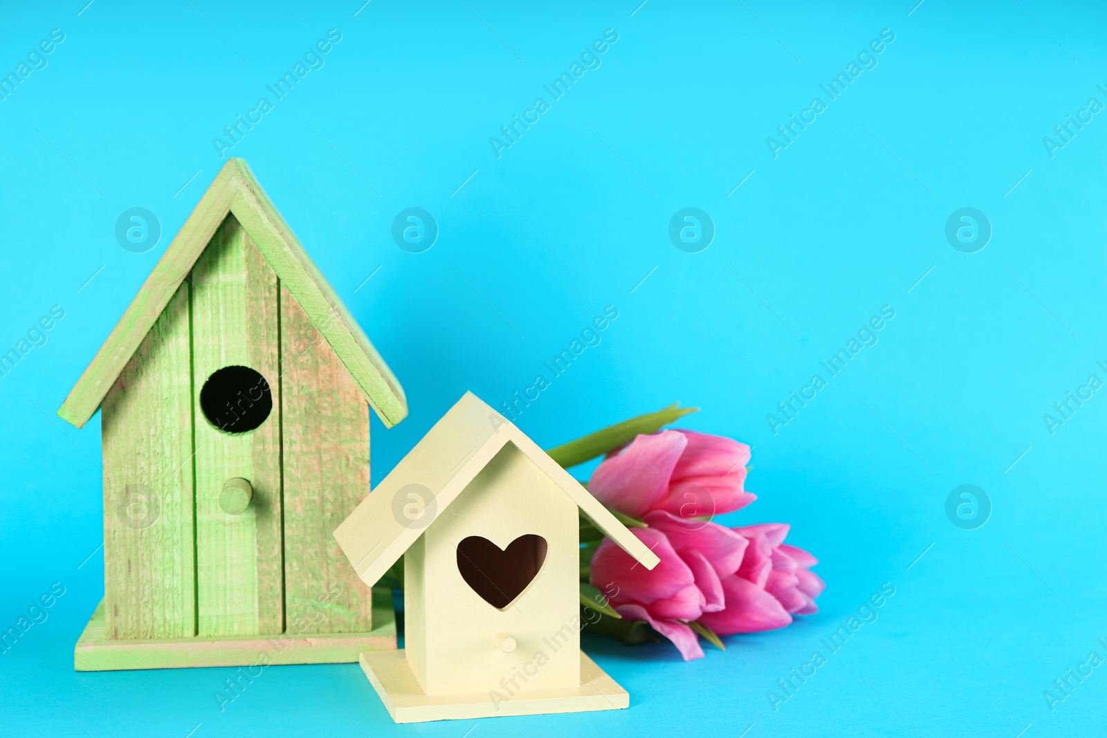 Photo of Beautiful bird houses and pink tulips on light blue background, space for text