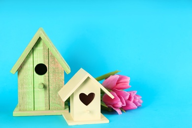 Photo of Beautiful bird houses and pink tulips on light blue background, space for text