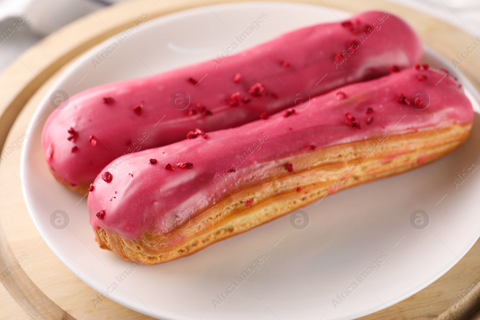 Photo of Plate with tasty glazed eclairs on wooden board, closeup