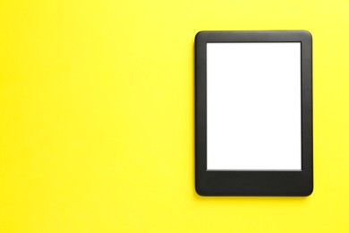 Photo of Modern e-book reader with blank screen on yellow background, top view. Space for text