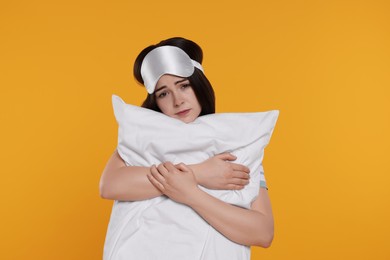 Photo of Unhappy young woman with sleep mask and pillow on yellow background. Insomnia problem