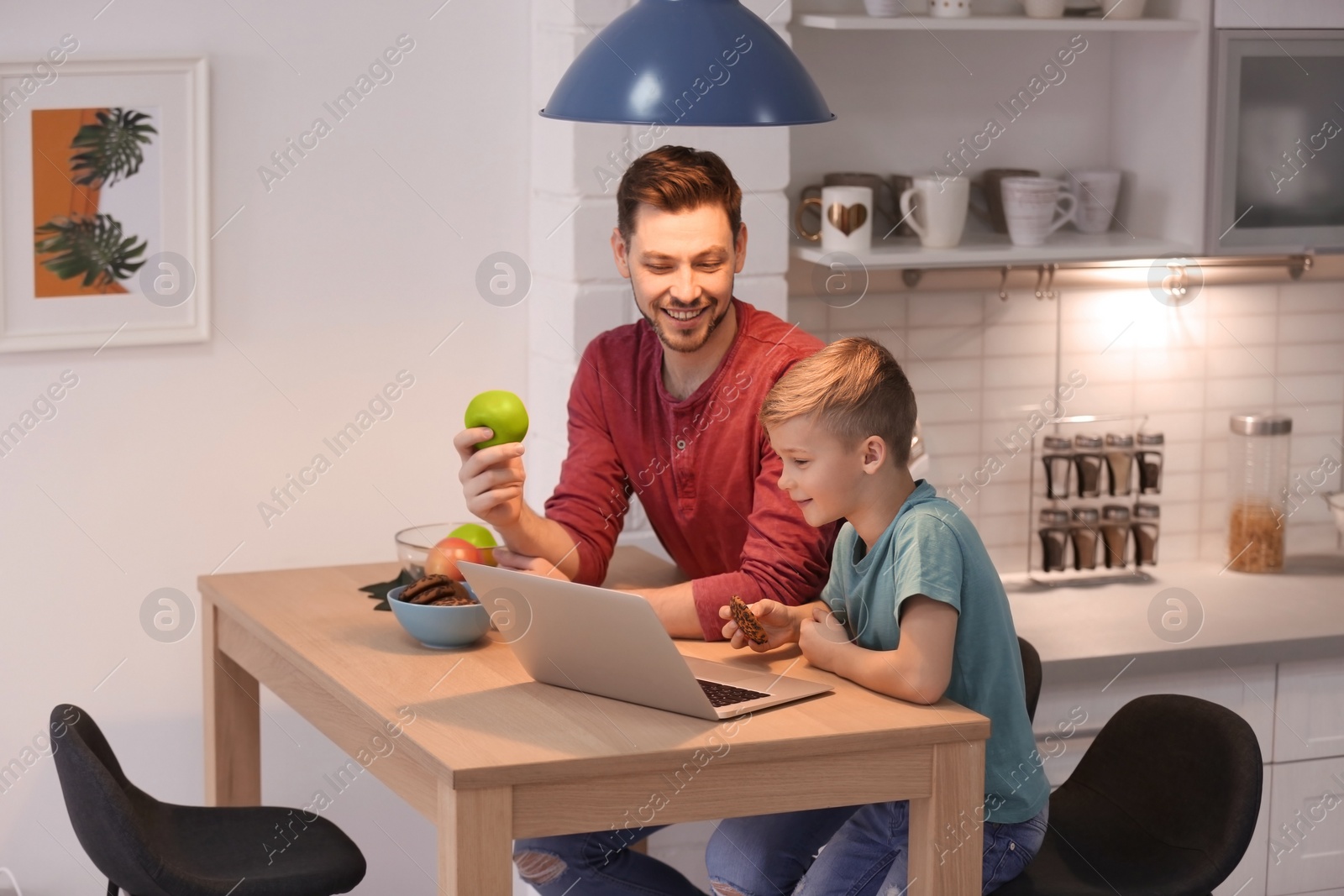 Photo of Little boy and his dad using laptop at home