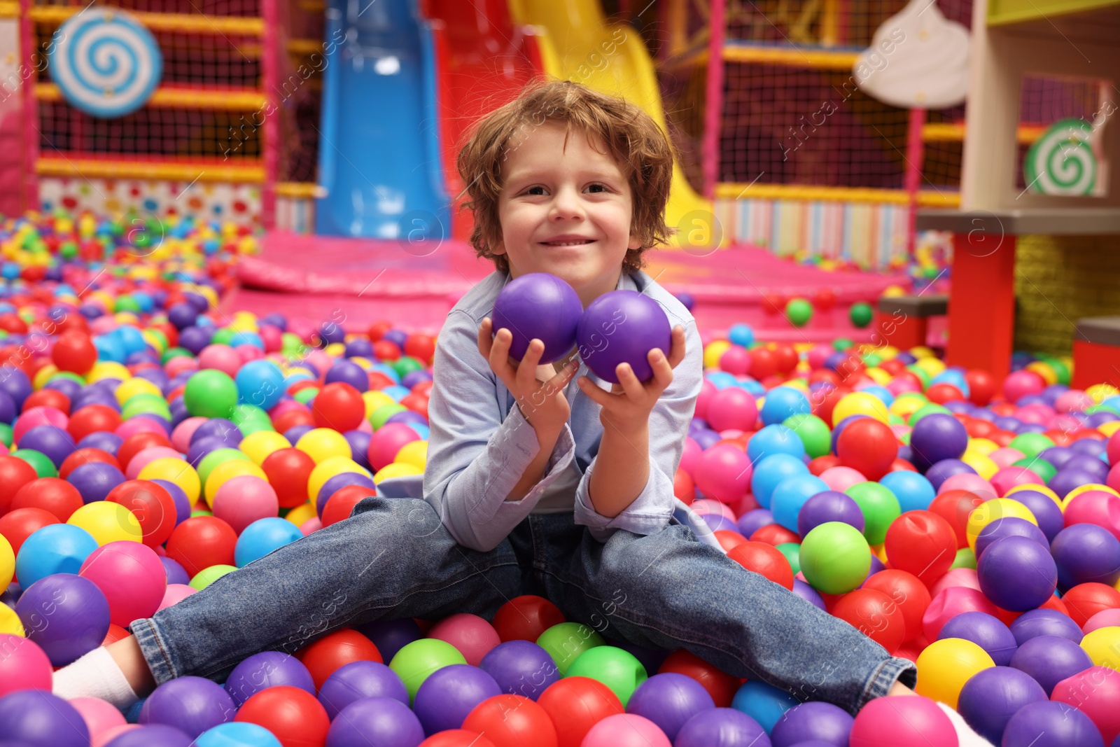 Photo of Happy little boy holding colorful balls in ball pit