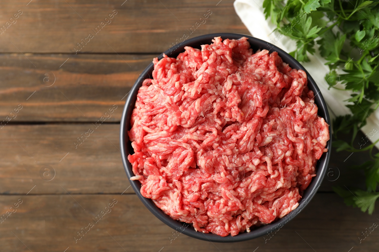 Photo of Raw ground meat in bowl and parsley on wooden table, top view. Space for text