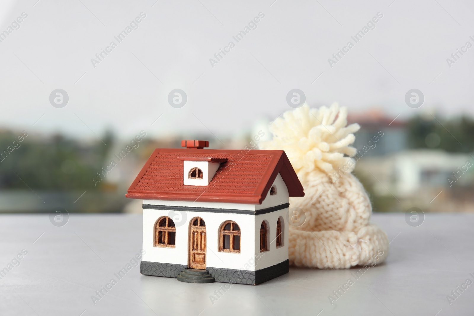 Photo of House model with knitted hat on table against blurred background. Heating concept