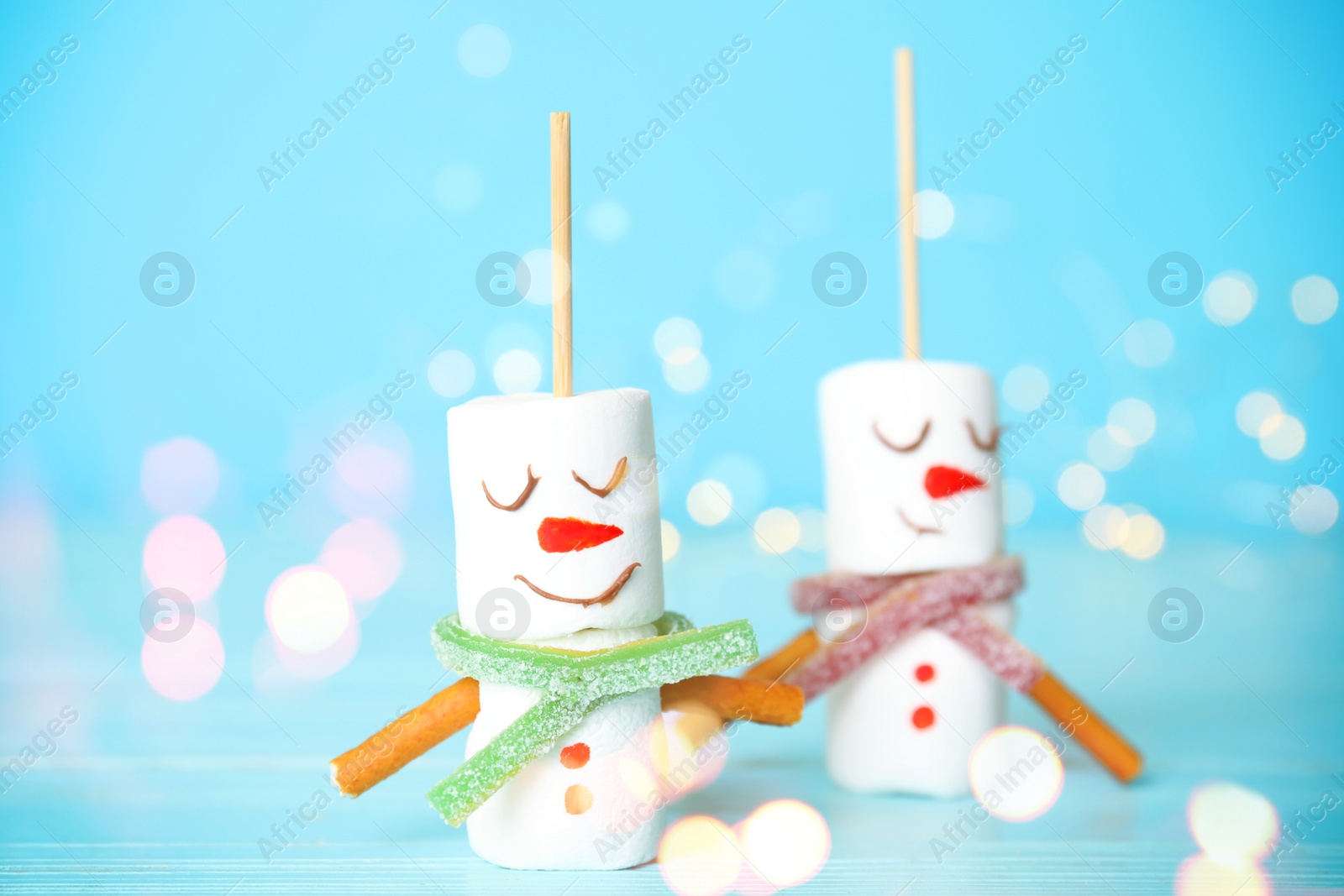 Image of Funny snowmen made of marshmallows on light blue background, closeup. Bokeh effect 