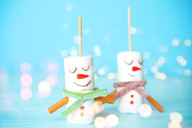 Image of Funny snowmen made of marshmallows on light blue background, closeup. Bokeh effect 