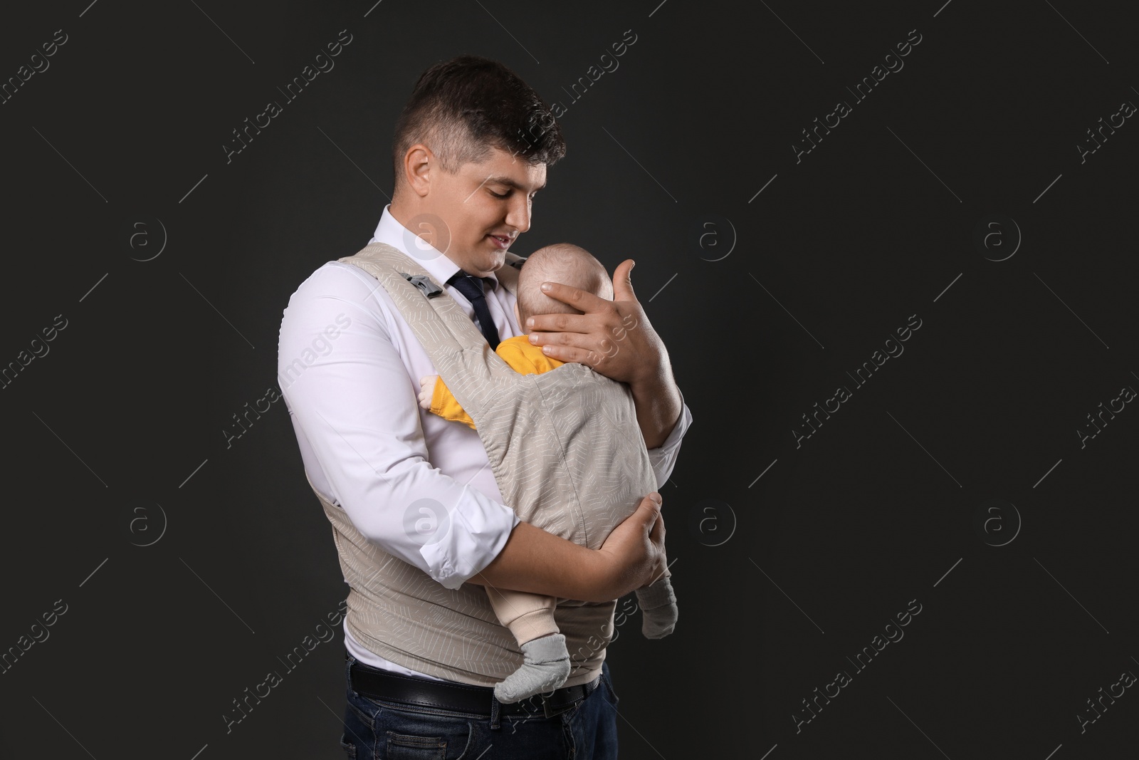 Photo of Father holding his child in baby carrier on black background. Space for text