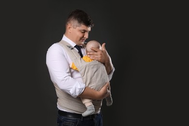 Photo of Father holding his child in baby carrier on black background. Space for text