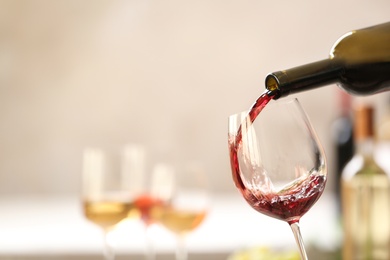 Photo of Pouring red wine from bottle into glass on blurred background. Space for text