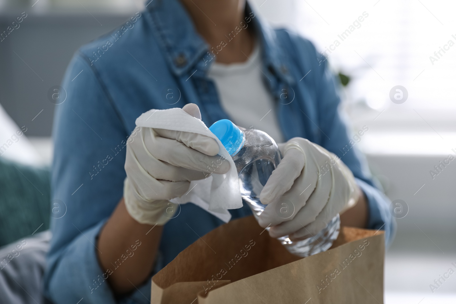 Photo of Woman cleaning bottle of water with wet wipe indoors, closeup