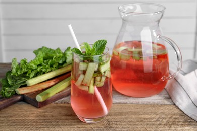 Tasty rhubarb cocktail and stems on wooden table