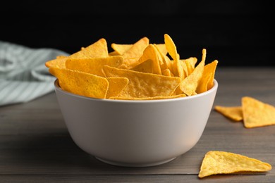 Photo of Tortilla chips (nachos) in bowl on wooden table against dark background, closeup