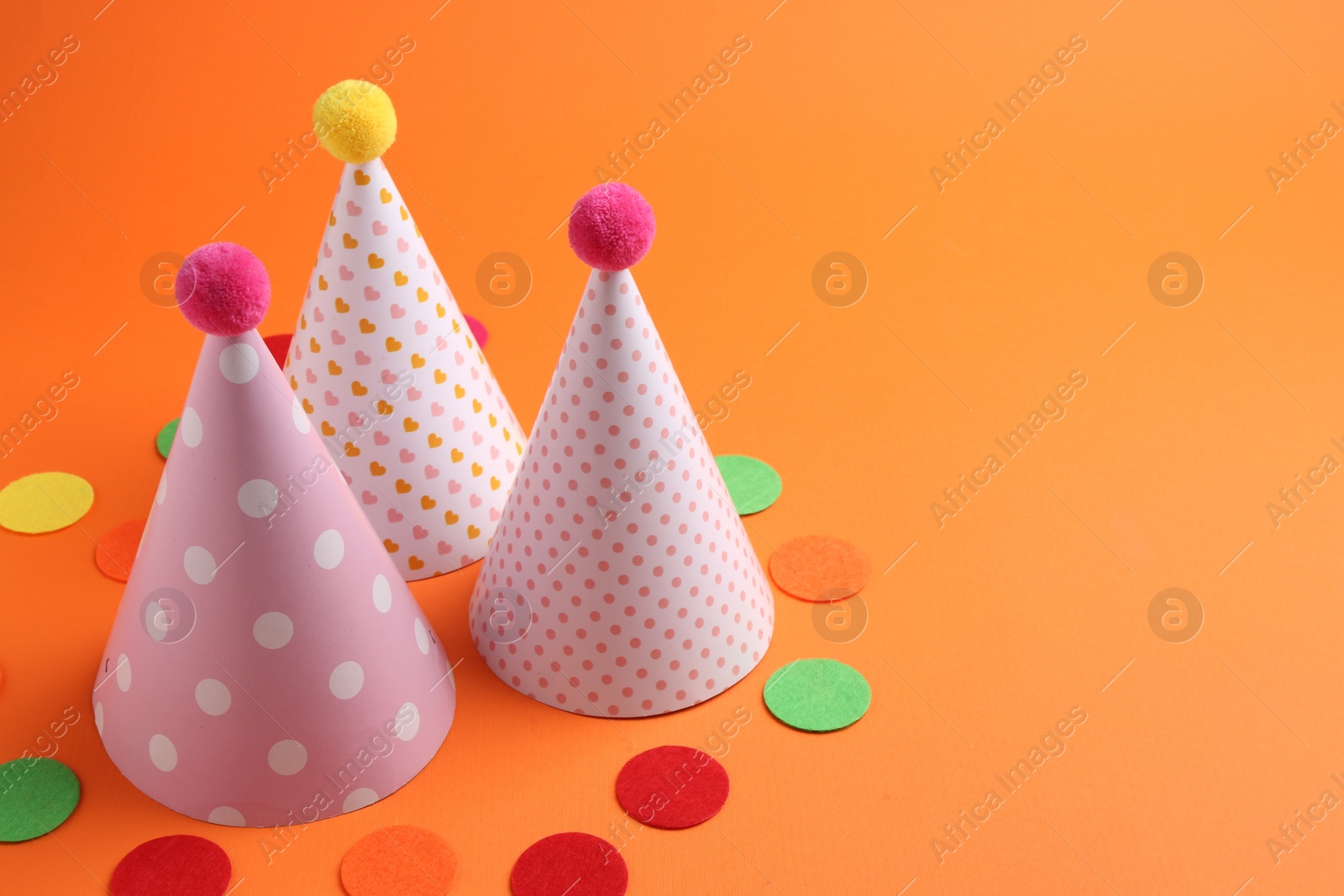 Photo of Party hats and colorful confetti on orange background. Space for text