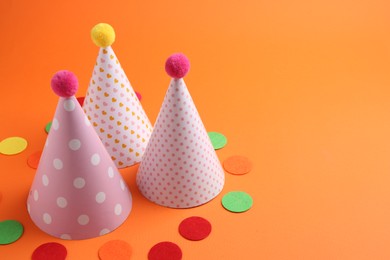 Party hats and colorful confetti on orange background. Space for text