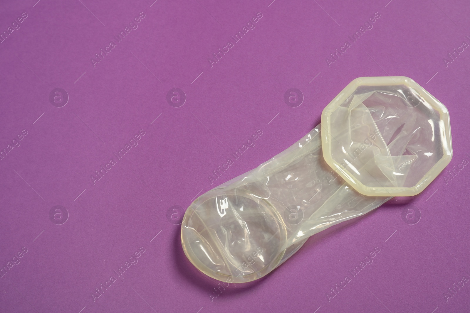 Photo of Unrolled female condom on violet background, top view and space for text. Safe sex