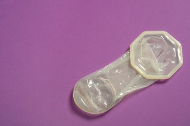 Unrolled female condom on violet background, top view and space for text. Safe sex