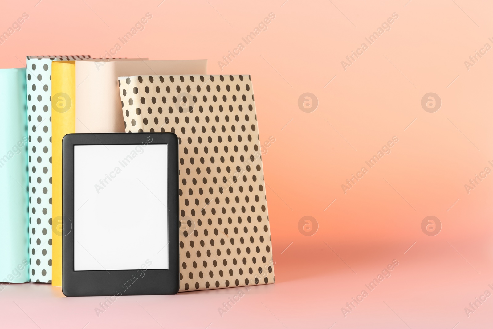 Photo of Modern e-book reader and hard cover books on pink background. Space for text