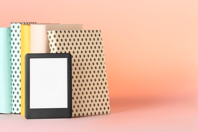 Photo of Modern e-book reader and hard cover books on pink background. Space for text